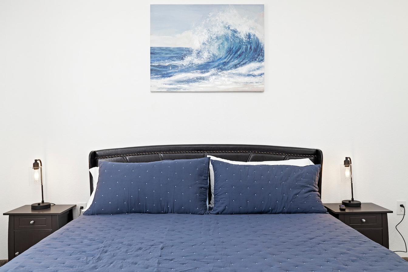 Master bedroom — crashing wave painting above tufted headboard